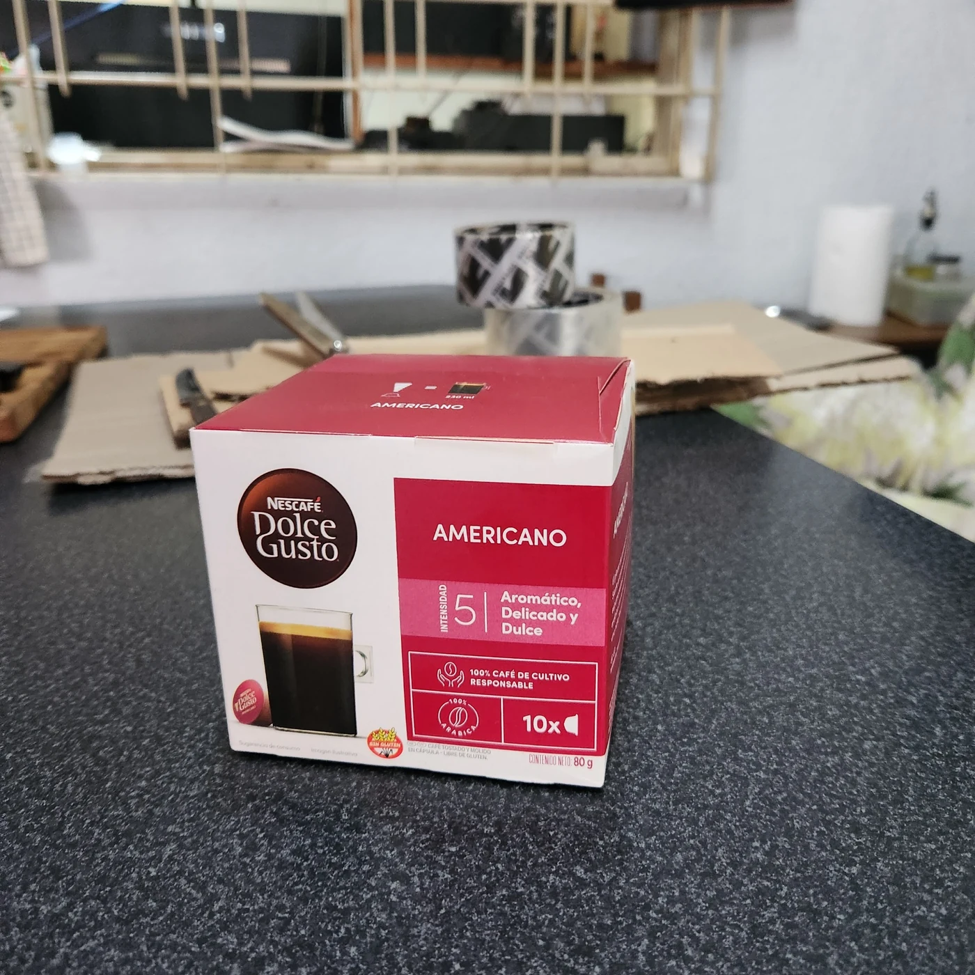 Fotografía doméstica de una caja de cápsulas de café sobre una mesa, utilizada como material inicial de demostración.